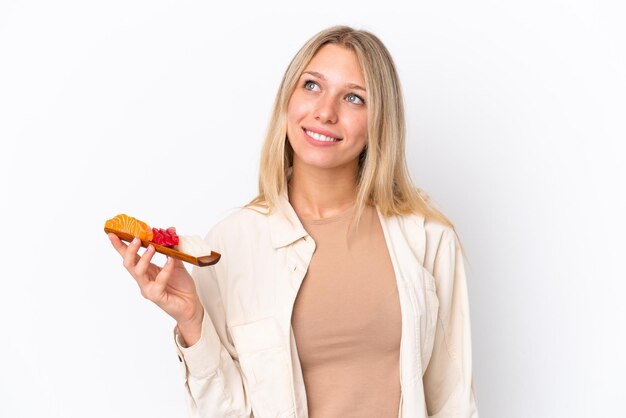 Giovane donna caucasica che tiene sashimi isolato su sfondo bianco pensando a un'idea mentre alza lo sguardo