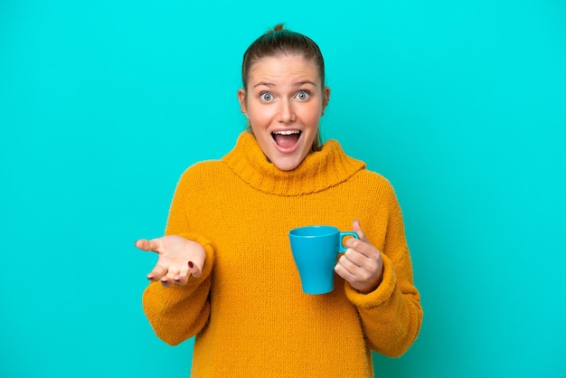 Giovane donna caucasica che tiene tazza isolata su sfondo blu con espressione facciale scioccata