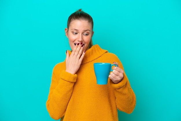 Giovane donna caucasica che tiene tazza isolata su sfondo blu con espressione facciale sorpresa e scioccata