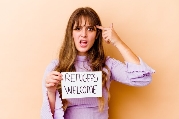 Giovane donna caucasica che tiene un cartello di benvenuto ai rifugiati isolato che mostra un gesto di delusione con l'indice.