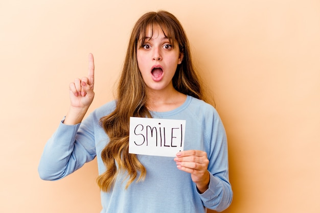 Giovane donna caucasica che tiene un cartello di sorriso isolato avendo qualche grande idea, concetto di creatività.