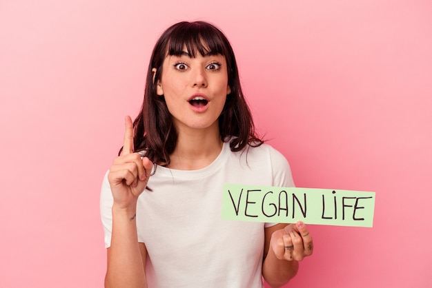 Giovane donna caucasica che tiene un cartello di vita vegano isolato su sfondo rosa con un'idea, un concetto di ispirazione.