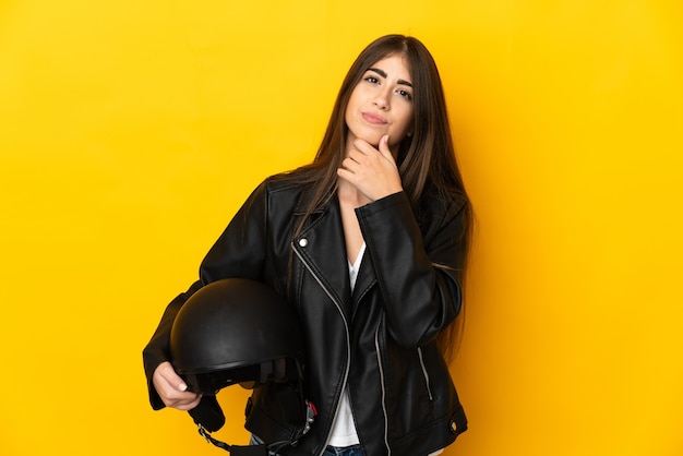 Giovane donna caucasica che tiene un casco del motociclo isolato su priorità bassa gialla e che osserva in su