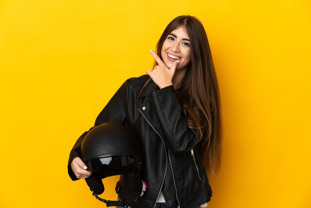 Giovane donna caucasica che tiene un casco del motociclo isolato su priorità bassa gialla felice e sorridente