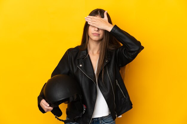 Giovane donna caucasica che tiene un casco del motociclo isolato su sfondo giallo che copre gli occhi con le mani. Non voglio vedere qualcosa