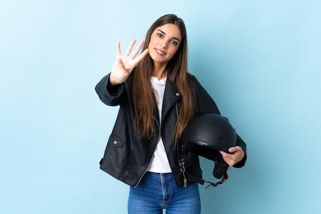 Giovane donna caucasica che tiene un casco del motociclo isolato sull'azzurro felice e contando quattro con le dita