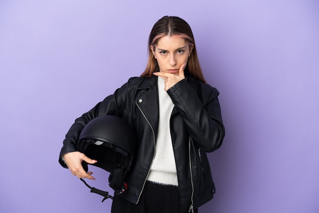 Giovane donna caucasica che tiene un casco del motociclo sul pensiero viola
