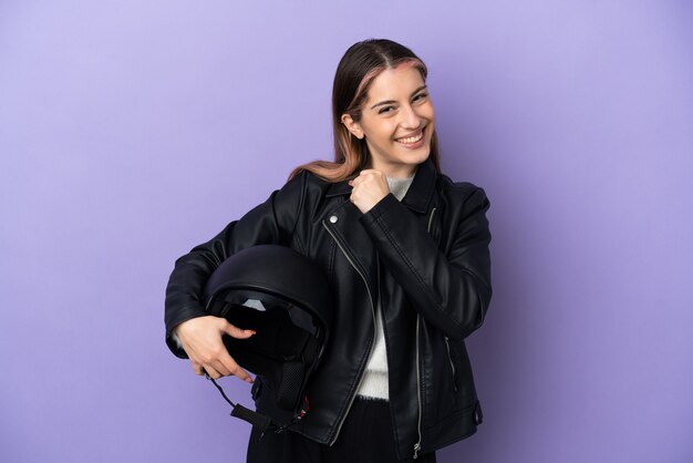 Giovane donna caucasica che tiene un casco del motociclo sulla porpora che celebra una vittoria