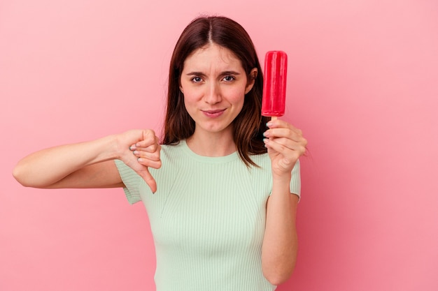 Giovane donna caucasica che tiene un gelato isolato su sfondo blu che mostra un gesto di antipatia, pollice verso. Concetto di disaccordo.