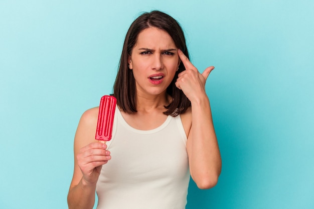 Giovane donna caucasica che tiene un gelato isolato su sfondo blu che mostra un gesto di delusione con l'indice.