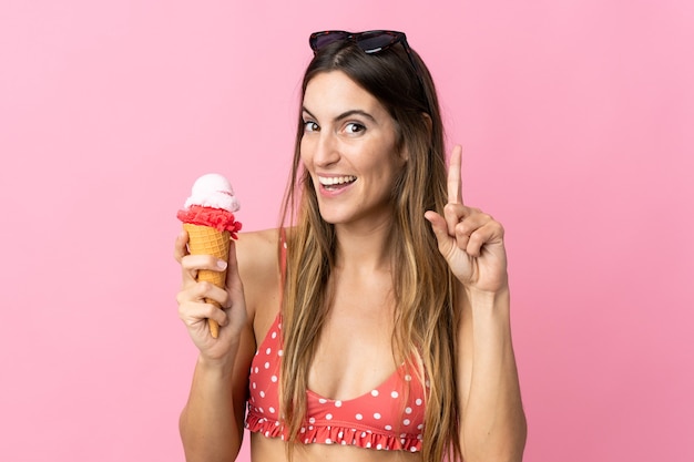 Giovane donna caucasica che tiene un gelato isolato su sfondo rosa che indica una grande idea