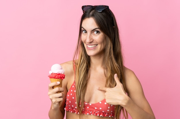 Giovane donna caucasica che tiene un gelato isolato su sfondo rosa con espressione facciale a sorpresa