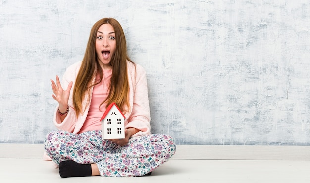 Giovane donna caucasica che tiene un'icona della casa che celebra una vittoria o un successo