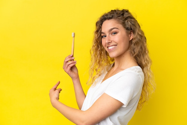 Giovane donna caucasica che tiene un lavarsi i denti isolato su sfondo giallo che punta indietro