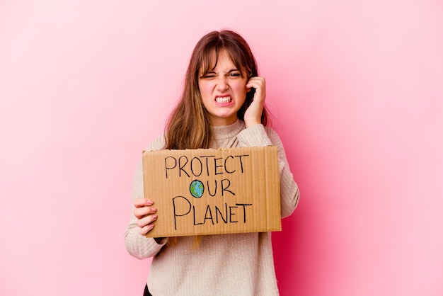 Giovane donna caucasica che tiene un Proteggere il nostro pianeta cartello isolato che copre le orecchie con le mani.