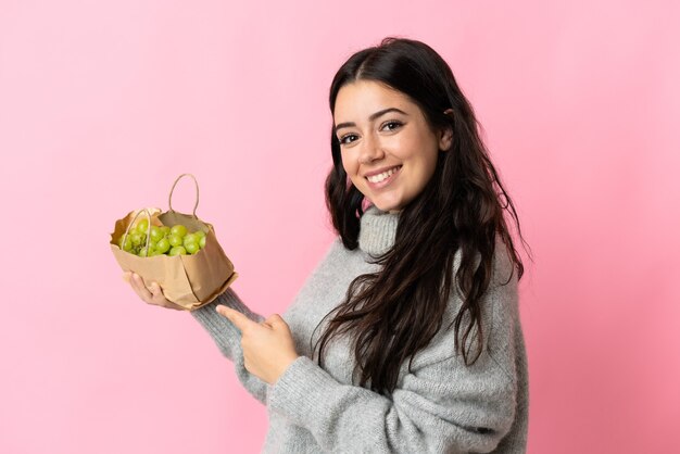 Giovane donna caucasica che tiene un'uva isolata sulla parete blu e la punta