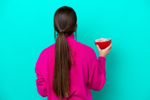 Giovane donna caucasica che tiene una ciotola di cereali isolata su sfondo blu nella posizione posteriore