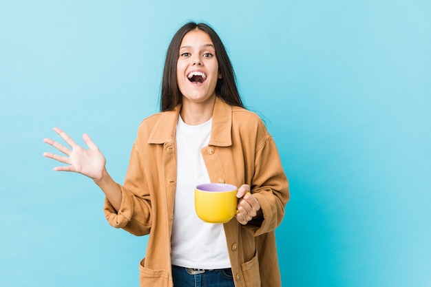 Giovane donna caucasica che tiene una tazza di caffè che celebra una vittoria o un successo