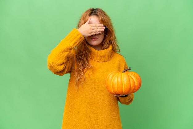 Giovane donna caucasica che tiene una zucca isolata su sfondo verde chroma key che copre gli occhi con le mani Non voglio vedere qualcosa