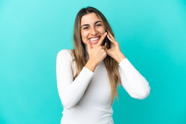 Giovane donna caucasica che utilizza il telefono cellulare isolato su sfondo blu felice e sorridente