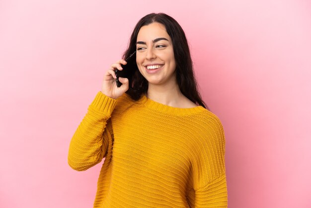 Giovane donna caucasica che utilizza il telefono cellulare isolato su sfondo rosa guardando di lato e sorridente