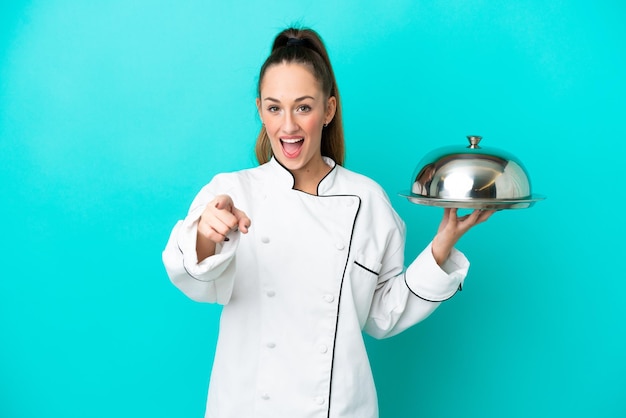 Giovane donna caucasica chef con vassoio isolato su sfondo blu sorpreso e rivolto verso la parte anteriore