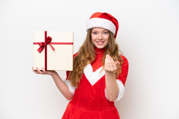 Giovane donna caucasica con abito natalizio in possesso di regalo isolato su sfondo bianco che invita a venire con la mano Felice che tu sia venuto