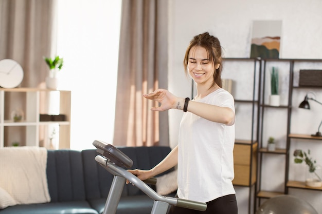 Giovane donna caucasica con braccialetto fitness facendo esercizi cardio su un tapis roulant a casa