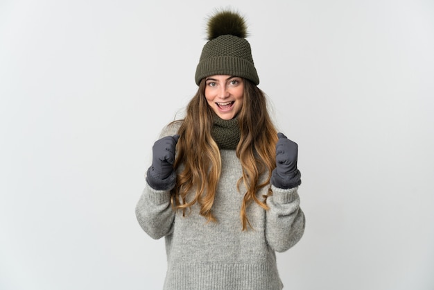 Giovane donna caucasica con cappello invernale su bianco che celebra una vittoria nella posizione del vincitore