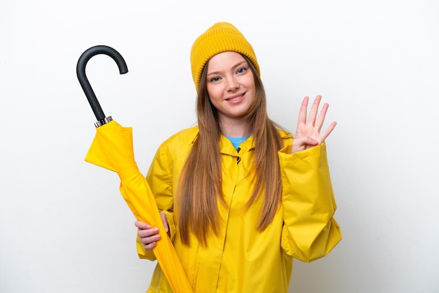 Giovane donna caucasica con cappotto antipioggia e ombrello isolati su sfondo bianco felice e contando quattro con le dita