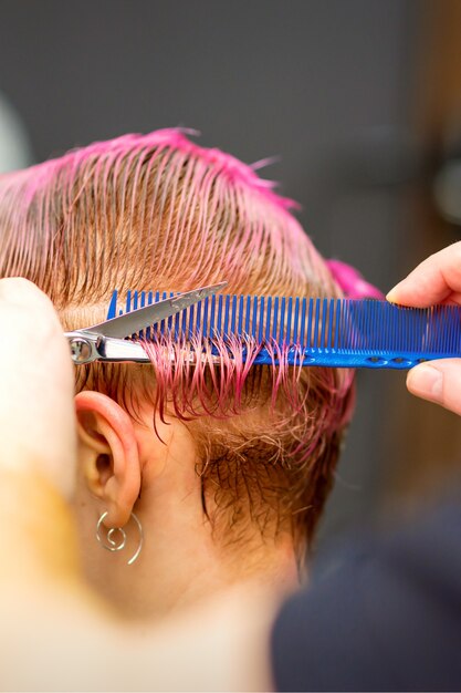 Giovane donna caucasica con i capelli rosa che si fa un taglio di capelli corto da un parrucchiere maschio con le mani in un parrucchiere