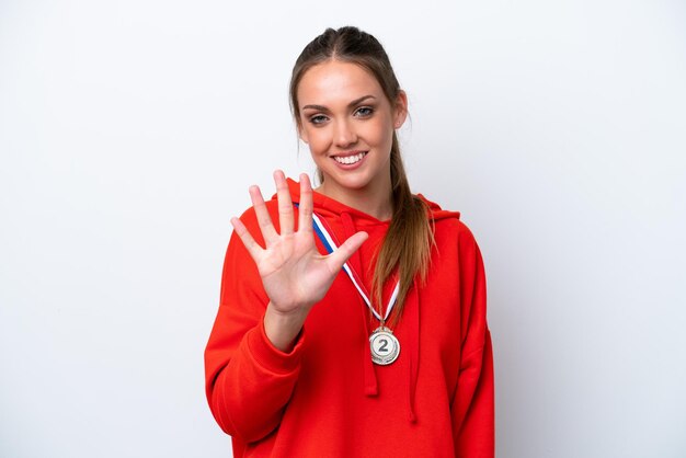 Giovane donna caucasica con medaglie isolate su sfondo bianco contando cinque con le dita