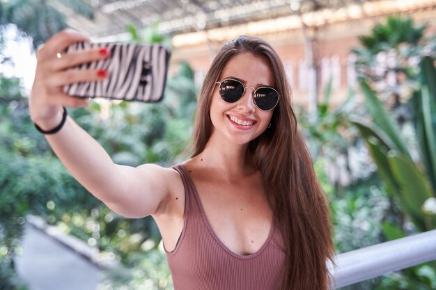 Giovane donna caucasica con occhiali da sole e capelli lunghi che si fa un selfie con uno smartphone