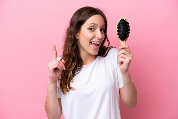 Giovane donna caucasica con pettine per capelli isolato su sfondo rosa che indica una grande idea