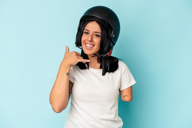 Giovane donna caucasica con un braccio che indossa un casco da motociclista isolato o sfondo blu che mostra un gesto di telefonata con le dita.