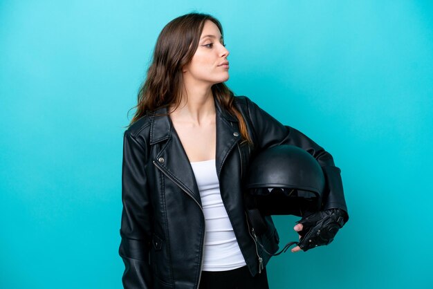 Giovane donna caucasica con un casco da motociclista isolato su sfondo blu che guarda al lato