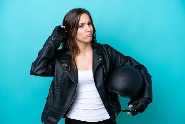 Giovane donna caucasica con un casco da motociclista isolato su sfondo blu che ha dei dubbi