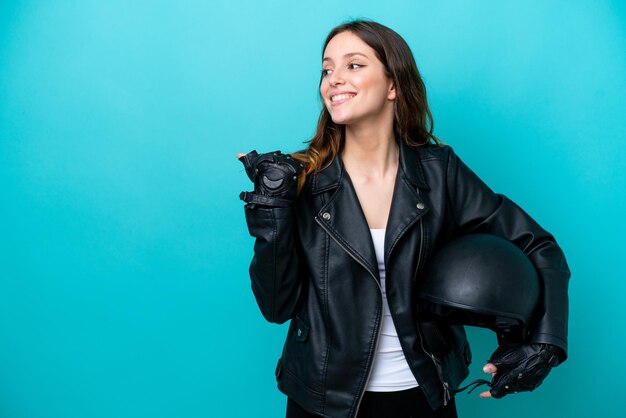 Giovane donna caucasica con un casco da motociclista isolato su sfondo blu che indica il lato per presentare un prodotto