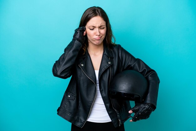 Giovane donna caucasica con un casco da motociclista isolato su sfondo blu frustrato e che copre le orecchie