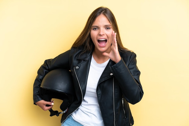 Giovane donna caucasica con un casco da motociclista isolato su sfondo giallo che grida con la bocca spalancata