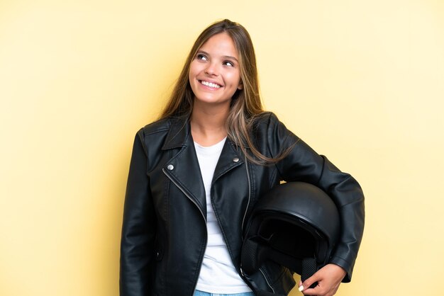 Giovane donna caucasica con un casco da motociclista isolato su sfondo giallo che pensa a un'idea mentre guarda in alto