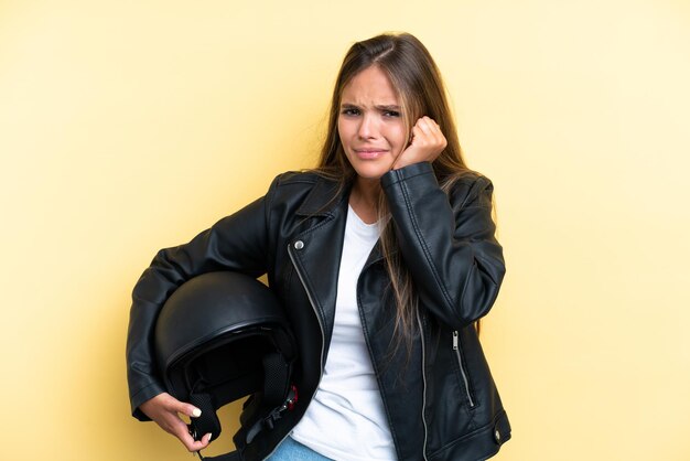 Giovane donna caucasica con un casco da motociclista isolato su sfondo giallo frustrato e che copre le orecchie