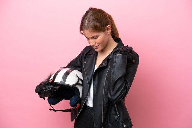 Giovane donna caucasica con un casco da motociclista isolato su sfondo rosa che soffre di dolore alla spalla per aver fatto uno sforzo