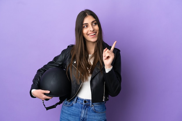 Giovane donna caucasica con un casco da motociclista isolato su sfondo viola che indica una grande idea