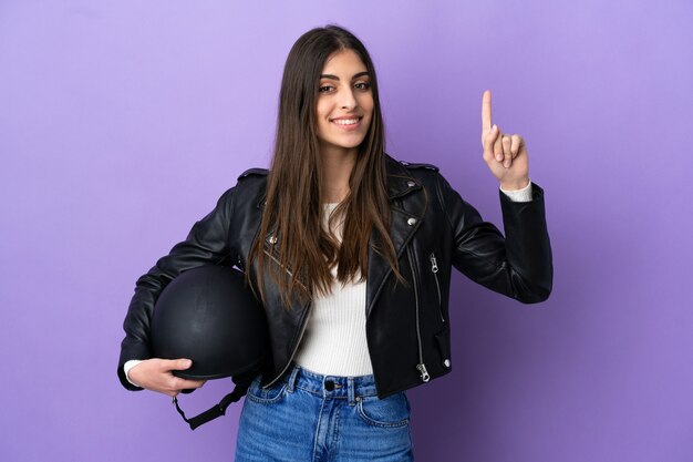 Giovane donna caucasica con un casco da motociclista isolato su sfondo viola che indica una grande idea