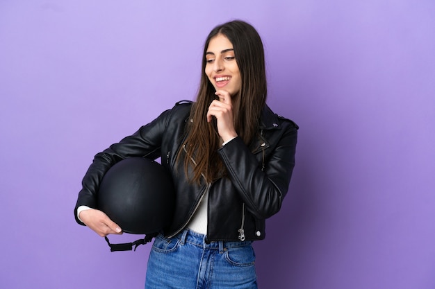 Giovane donna caucasica con un casco da motociclista isolato su sfondo viola guardando di lato e sorridente