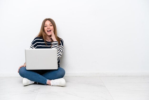 Giovane donna caucasica con un computer portatile seduto sul pavimento isolato su sfondo bianco con espressione facciale sorpresa e scioccata