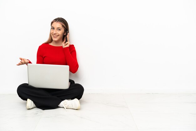 Giovane donna caucasica con un computer portatile seduto sul pavimento mantenendo una conversazione con il telefono cellulare con qualcuno