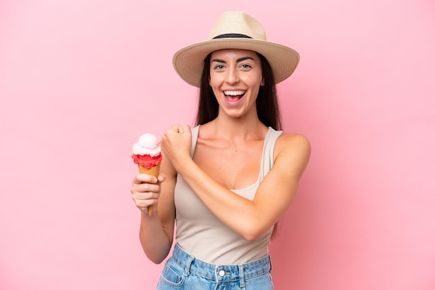 Giovane donna caucasica con un gelato alla cornetta isolato su sfondo rosa che celebra una vittoria