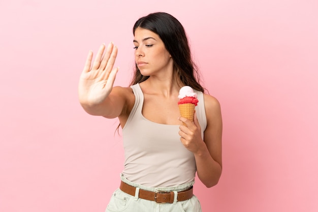 Giovane donna caucasica con un gelato alla cornetta isolato su sfondo rosa che fa un gesto di arresto e deluso